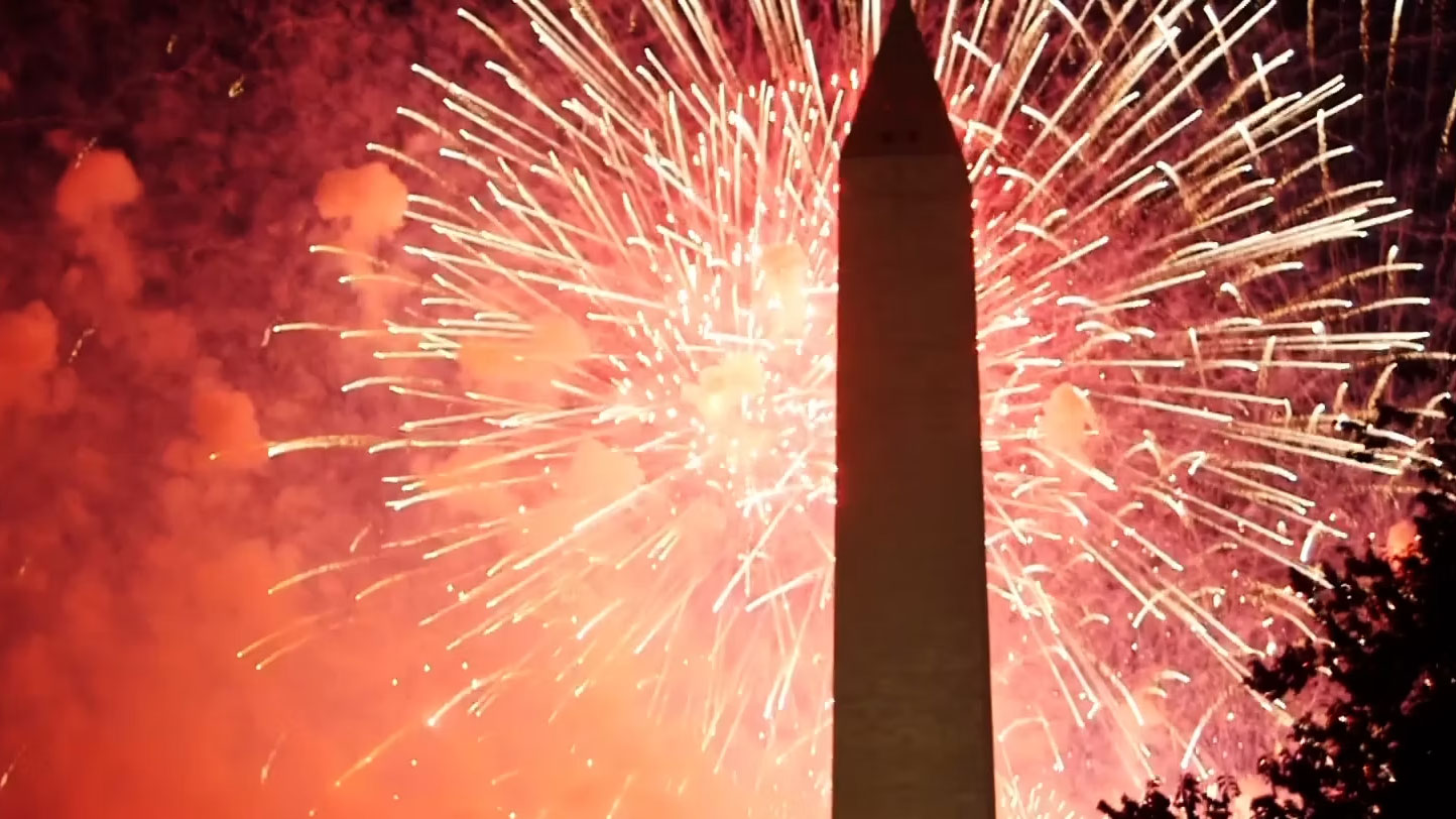 Red and yellow fireworks burst behind a silhouette of the Washington Monument.