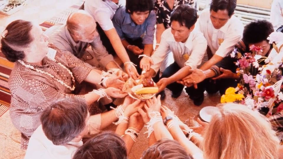 A group of people sit on the ground in a circle, each readhing their arms out a plate of food.