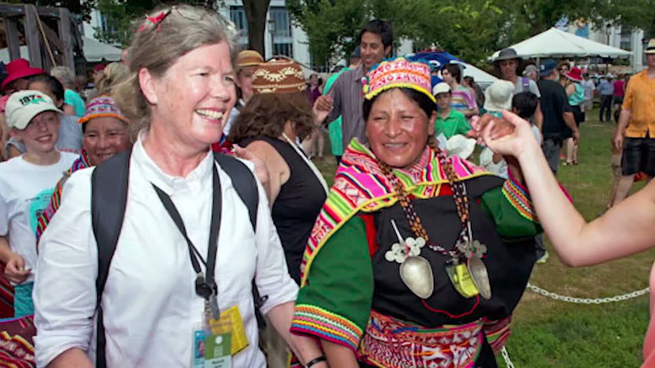 Two women, one in Western dress clothes and the other in brightly colored, embroidered dress of Central or South America.