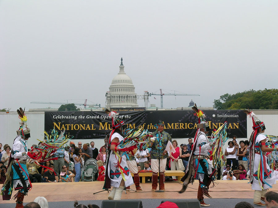 Native dancers perform on an outdoor stage with the U.S. Capitol Building in the background.