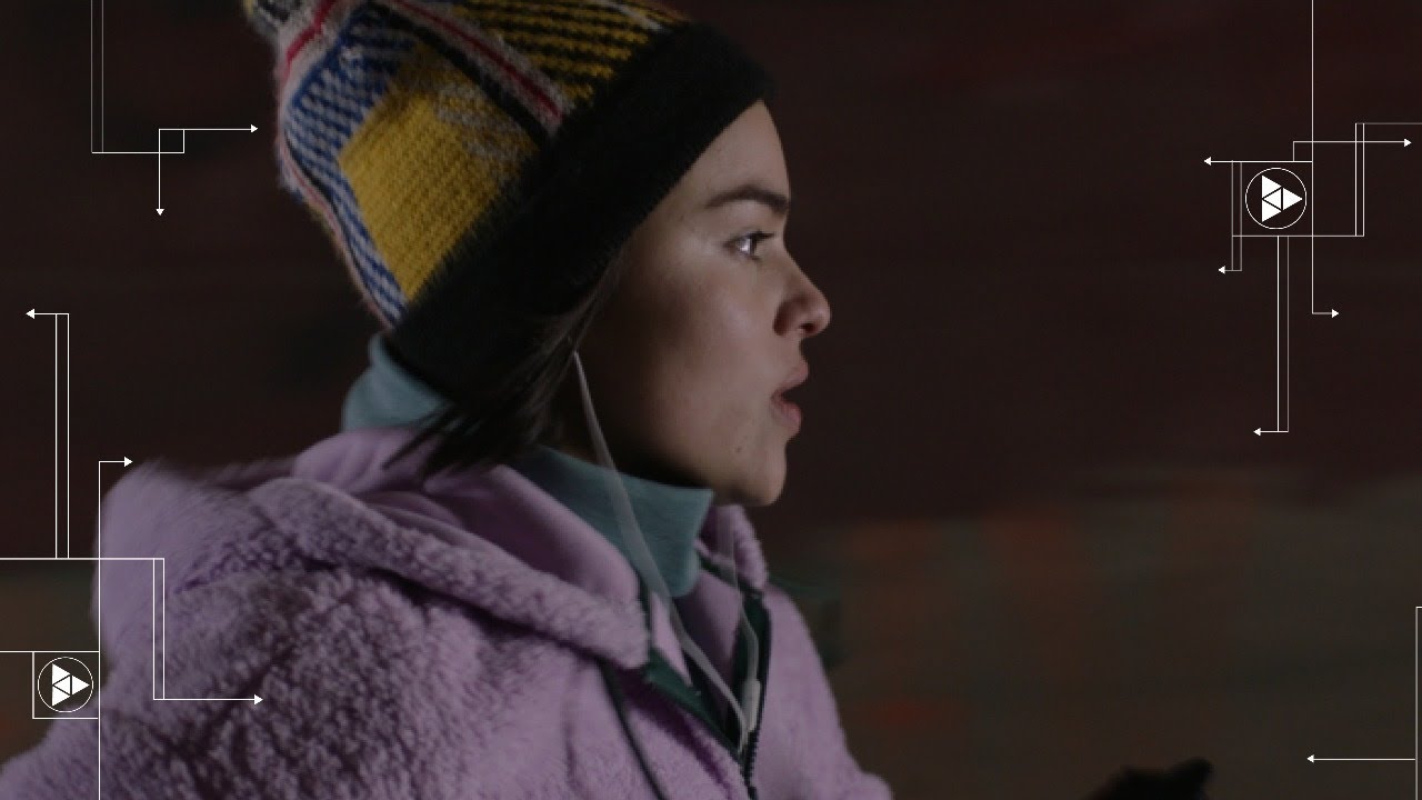 Film still of young woman in profile, wearing beanie and pink fuzzy coat.